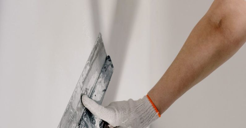 DIY Projects - Crop anonymous male worker in gloves holding putty knife while working at home