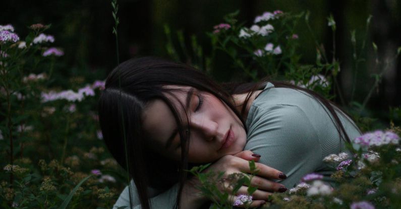 Vertical Gardens - Young female with dark hair embracing herself and putting head on hands sitting on squat in grass with blooming meadow flowers in park